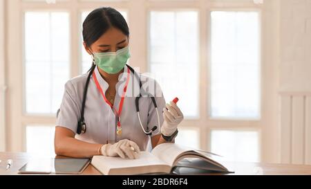 Photo de la jeune femme qui travaille comme médecin portant un stéthoscope et assis à la table en bois avec livre et tablette d'ordinateur sur l'offique ordonné du médecin Banque D'Images