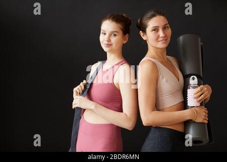 Portrait de deux jeunes femmes belles souriantes à l'appareil photo sur fond noir, elles sont prêtes pour l'entraînement sportif Banque D'Images