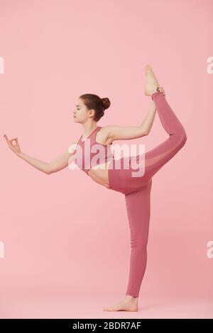 Vue latérale de la jeune femme mince faisant des exercices d'étirements et pratiquant le yoga sur fond rose Banque D'Images