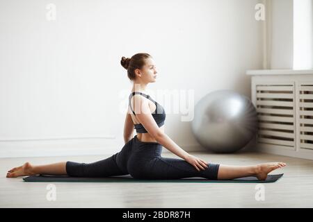 Jeune femme flexible assise sur les fentes sur le tapis d'exercice pendant l'entraînement sportif Banque D'Images