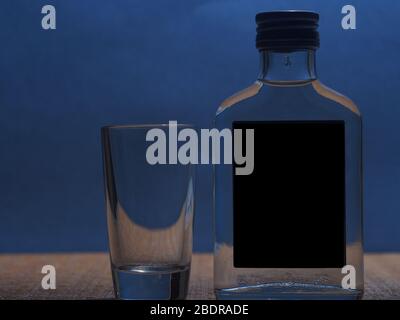 Silhouette d'une petite bouteille de verre avec vodka et d'une pile de verre sur un fond bleu. La vie-fixe. Banque D'Images