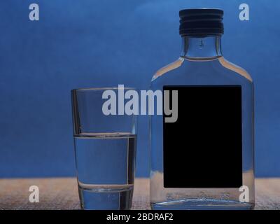 Silhouette d'une petite bouteille de verre avec vodka et d'une pile de verre sur un fond bleu. La vie-fixe. Banque D'Images