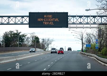 Message « ÉVITER LES DÉPLACEMENTS NON ESSENTIELS » sur un panneau de messages électroniques de circulation, au-dessus de la route et des voitures pendant la pandémie de COVID-19 Banque D'Images