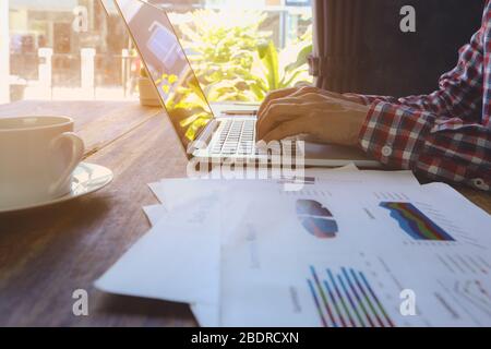 Gros plan de l'homme d'affaires décontracté, les mains dactylographiant sur l'ordinateur et assis sur le bureau en bois. Rapport financier recettes statistiques concept comptable. Banque D'Images