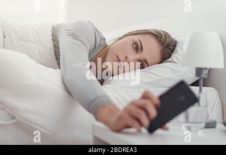 Femme de se réveiller dans son lit et prendre son smartphone, elle est la consultation des messages d'alarme et répétition Banque D'Images