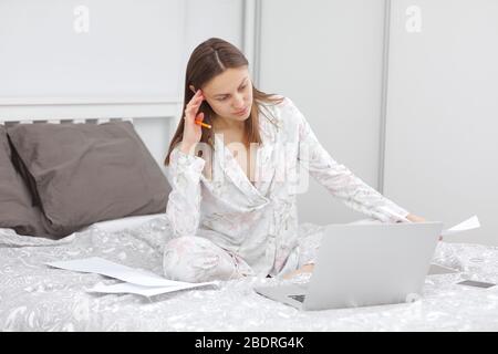 Une belle femme d'affaires qui travaillait sur un ordinateur portable sur le lit. Une fille qui s'est mise en quarantaine au bureau à domicile. Restez à la maison. Freelance. Communication et Banque D'Images