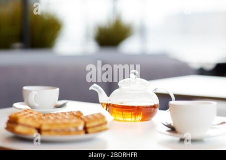 L'image de la théière avec tasses et gâteaux est sur la table préparée pour le petit déjeuner dans le café Banque D'Images