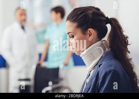 Jeune patiente avec col cervical à l'hôpital, elle est assise dans la salle d'attente, le personnel médical sur le fond Banque D'Images