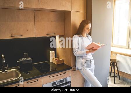 Femme de ménage caucasienne sérieuse regardant par un livre Banque D'Images