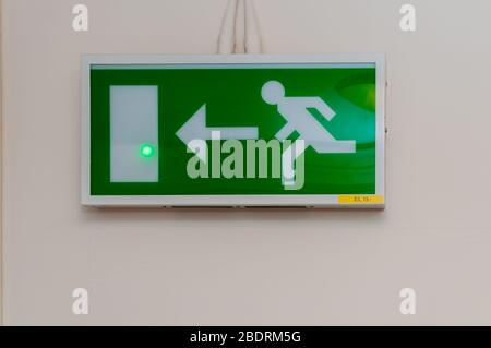 Une plaque de signalisation de sortie verte au néon avec un personnage désactivé, un personnage homme et une flèche vers la porte comme instructions pour les directions en cas d'urgence Banque D'Images