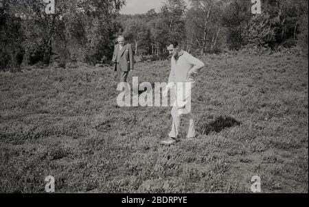 Années 60, historique, "dans le rugueux", pas un bon endroit pour être sur un parcours de golf, un golfeur et un homme dans un costume de trois pièces, regarder sur le terrain pour les joueurs manquant de balle de golf, Angleterre, Royaume-Uni. Un golfeur a seulement un certain nombre de minutes (était 5, maintenant seulement 3 minutes) pour rechercher et trouver sa balle de golf, sinon il doit revenir et frapper un autre coup de l'endroit où la balle originale a été dernier joué. Banque D'Images