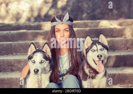 Jolie fille et ses animaux. Swag rapper femme avec ses chiens husky isolé urbain gris mur arrière-plan assis sur les escaliers les trois regardant vous cameraT Banque D'Images