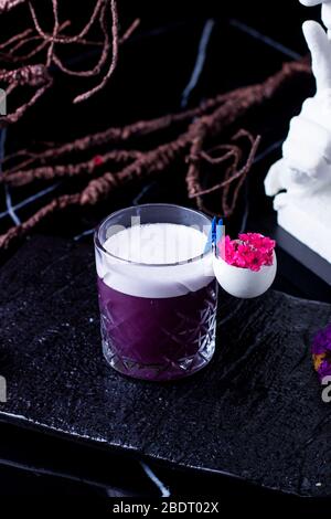 un verre de verre de violet de cocktail garni avec fleur dans la coquille d'oeuf Banque D'Images