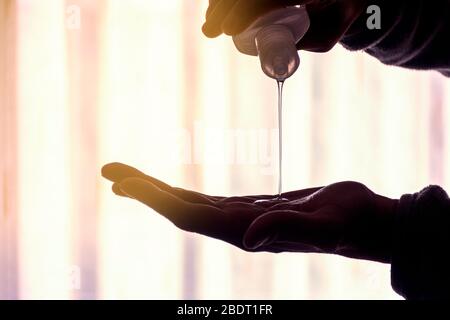 Un homme utilisant du gel désinfectant hydroalcoolique, tombant d'une bouteille sur sa main. Rétroéclairage du soleil Banque D'Images