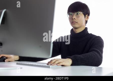 Bel homme chinois dans des verres travaillant au bureau. Fond blanc Banque D'Images