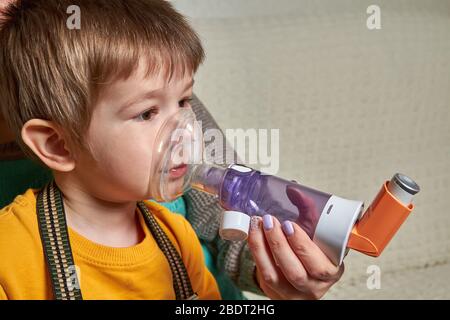 Un petit garçon souffrant d'asthme bronchique souffrant de maladie, qui reçoit un traitement respiratoire de la mère avec un inhalateur aérosol. Traitement des complications de vi Banque D'Images