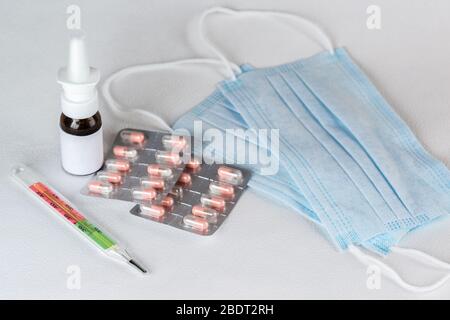 Deux masques médicaux jetables simples en tissu non tissé avec bandes élastiques, médicaments et thermomètre se trouvent sur une table blanche. Mise au point sélective Banque D'Images