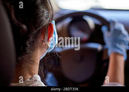Une jeune femme dans un masque chirurgical et des gants conduisant la voiture pendant la pandémie de coronavirus. Une femme conducteur en équipement de protection, empêchant l'infection Banque D'Images