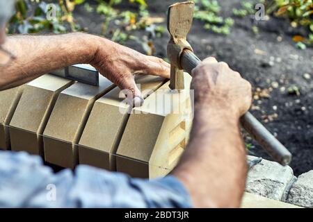 Bricklayer installer des briques sur la nouvelle clôture à partir de briques de face à l'aide d'un marteau. Banque D'Images