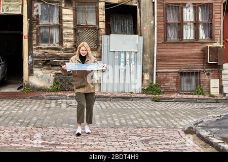 Jeune femme blanche de race blanche dans les manteaux de pluie marche à Istanbul et tient une carte topographique pour trouver son emplacement, parce qu'elle est touristique. Banque D'Images