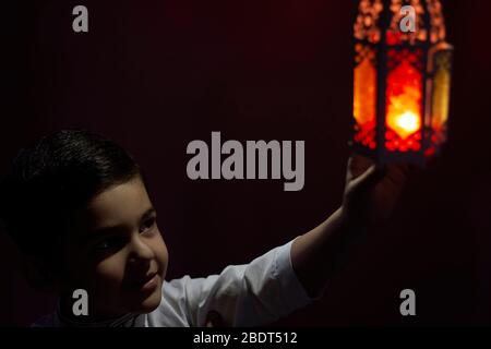 Un garçon musulman touche une bougie traditionnelle arabe à la lanterne qui souffle dans l'obscurité. Garçon du Moyen-Orient priant. Remercier dieu. Ramadan, concepts d'Eid-al-Adha Banque D'Images