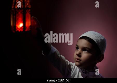 Un garçon musulman touche une bougie traditionnelle arabe à la lanterne qui souffle dans l'obscurité. Garçon du Moyen-Orient priant. Remercier dieu. Ramadan, concepts d'Eid-al-Adha Banque D'Images