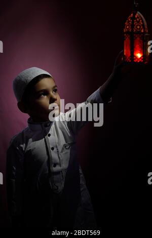 Un garçon musulman touche une bougie traditionnelle arabe à la lanterne qui souffle dans l'obscurité. Garçon du Moyen-Orient priant. Remercier dieu. Ramadan, concepts d'Eid-al-Adha Banque D'Images