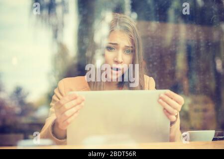 Choqué woman holding ordinateur, ordinateur portable écran de tablette à la surprise in coffee shop Banque D'Images