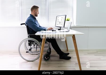 Homme d'handicapés assis sur fauteuil roulant et Using Computer in Office Banque D'Images