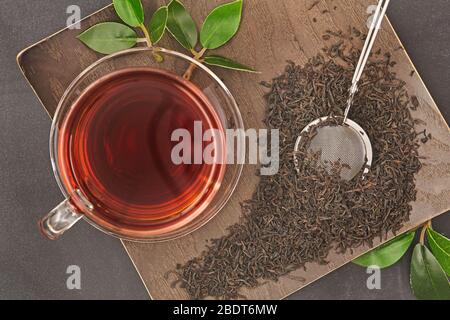 Tasse de thé chaud en verre sur feuilles de thé noir sec sur fond en bois. Vue de dessus. Banque D'Images