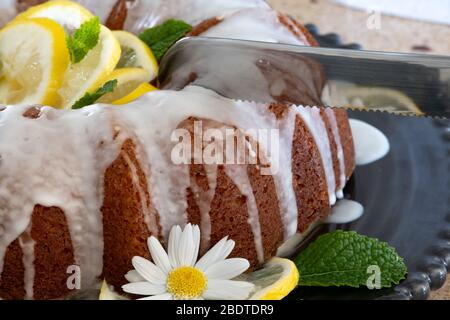 Un couteau passe dans un gâteau au limon ricotta avec glaçage affiché sur une plaque décorative noire avec des fleurs Daisy dans un vase en arrière-plan. Banque D'Images