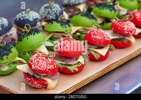 Trois mini hamburgers sur des petits pains colorés élevés en rouge, vert et noir sur un plateau. Banque D'Images