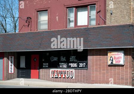 South Elgin, Illinois, États-Unis. Un magasin de deux étages situé sur le devant abrite un salon de tatouage et un salon de beauté le long d'une rue principale dans une petite ville de banlieue. Banque D'Images