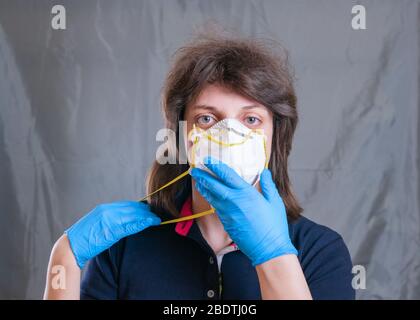 Jeune femme dans un masque respiratoire de protection et des gants bleus pendant l'auto-isolation et la quarantaine. Fond gris. Restez à la maison Banque D'Images