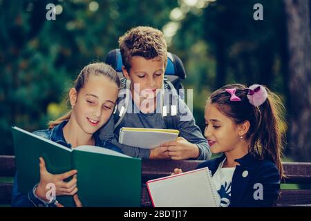 Retour à l'école. Les enfants avec des sacs à dos ont du plaisir, de parler, de lire un livre.Groupe d'écoliers élémentaires ayant une discussion sur les devoirs pendant leur déplacement Banque D'Images