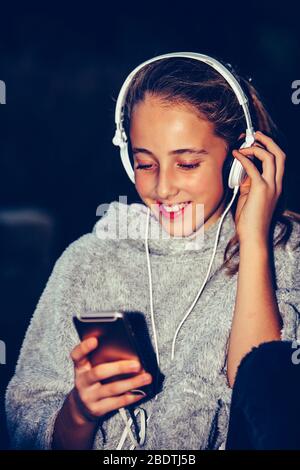 Portrait d'une heureuse adolescente écoutant de la musique en ligne avec des écouteurs d'un smartphone dans le parc Banque D'Images