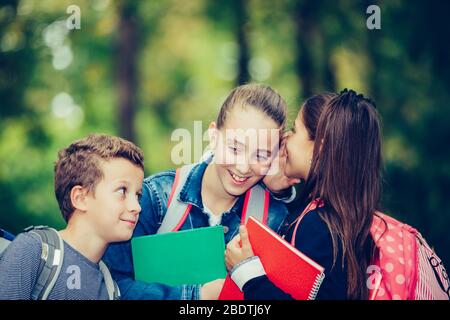 Fermez trois heureux amis avec des sacs à dos riant et s'amuser dans le parc. Garçon et fille tenant des livres le premier jour de l'école. Des enfants qui sont positifs Banque D'Images