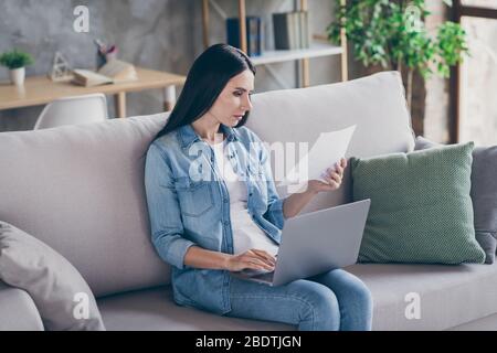 Portrait de elle belle jolie professionnelle bien focalisée professionnelle occupé brunet fille assis sur divan utilisant le document de lecture d'ordinateur portable dans le loft moderne Banque D'Images