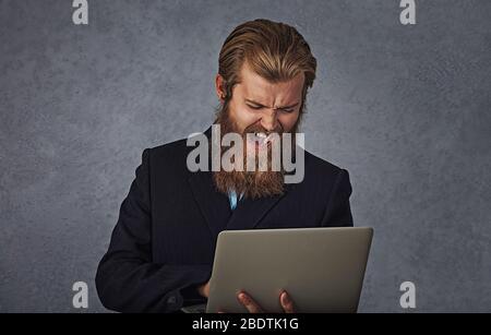 Homme d'affaires barbu tenant ordinateur criant isolé gris gris mur d'arrière-plan Banque D'Images