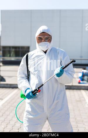 Désinfecteur dans un costume et un masque de protection, tenant les produits chimiques de désinfection à l'extérieur Banque D'Images
