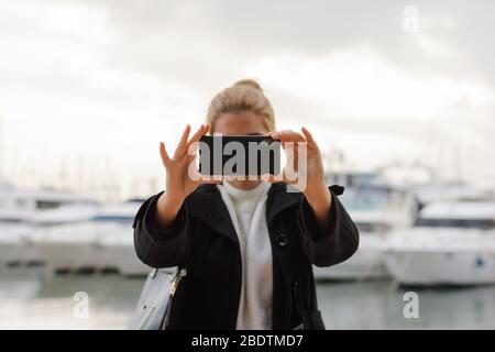 Une jeune femme prend une photo avec son smartphone en regardant l'appareil photo Banque D'Images