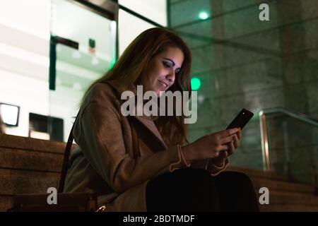 Une jeune femme écrit un message dans son smartphone dans la rue la nuit Banque D'Images