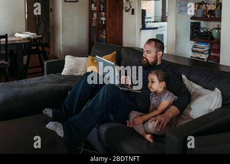 Père travaillant à la maison avec une jeune fille pendant l'isolement Banque D'Images