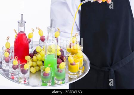 Gros plan d'un serveur tenant un plateau mélangeant la liqueur dans des verres avec du raisin. Service et cocktails végétaliens. Banque D'Images