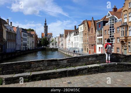 Une fille sur une pierre au-dessus du canal de Spiegelrei avec la tour de Poortersloge (Burgherss' Lodge) en arrière-plan.Bruges.Flandre Occidentale.Belgique Banque D'Images