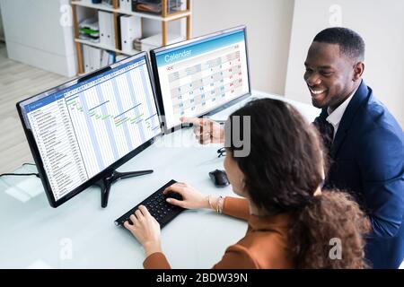 Young Businesspeople Analyse graphique de Gantt et Calendrier sur Computer in Office Banque D'Images