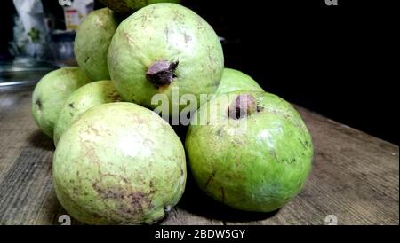 gros plan de la branche avec trois guavas vert mûrs sur fond de table en bois brun déchiré Banque D'Images