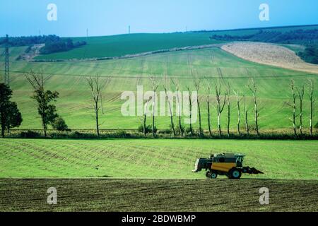 Paysage ensoleillé des champs verts sur les pentes et le tracteur labourage le sol Banque D'Images