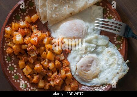 Sur des œufs moyens avec des pommes de terre et chorizo ou huevos estrellados con papas y chorizo, sur une plaque de boue ou d'argile mexicaine dans le cadre d'un petit déjeuner mexicain. Banque D'Images