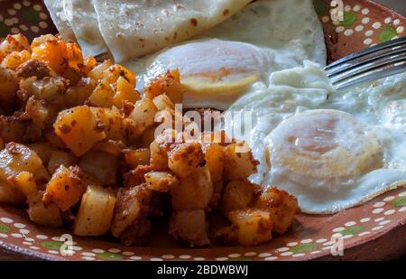 Sur des œufs moyens avec des pommes de terre et chorizo ou huevos estrellados con papas y chorizo, sur une plaque de boue ou d'argile mexicaine dans le cadre d'un petit déjeuner mexicain. Banque D'Images